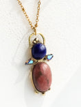 Load image into Gallery viewer, Close-up of handmade brass pendant featuring rhodonite cabochon, lapis lazuli stone and Swarovski comet crystal accents, bykjones artisan jewelry North Carolina
