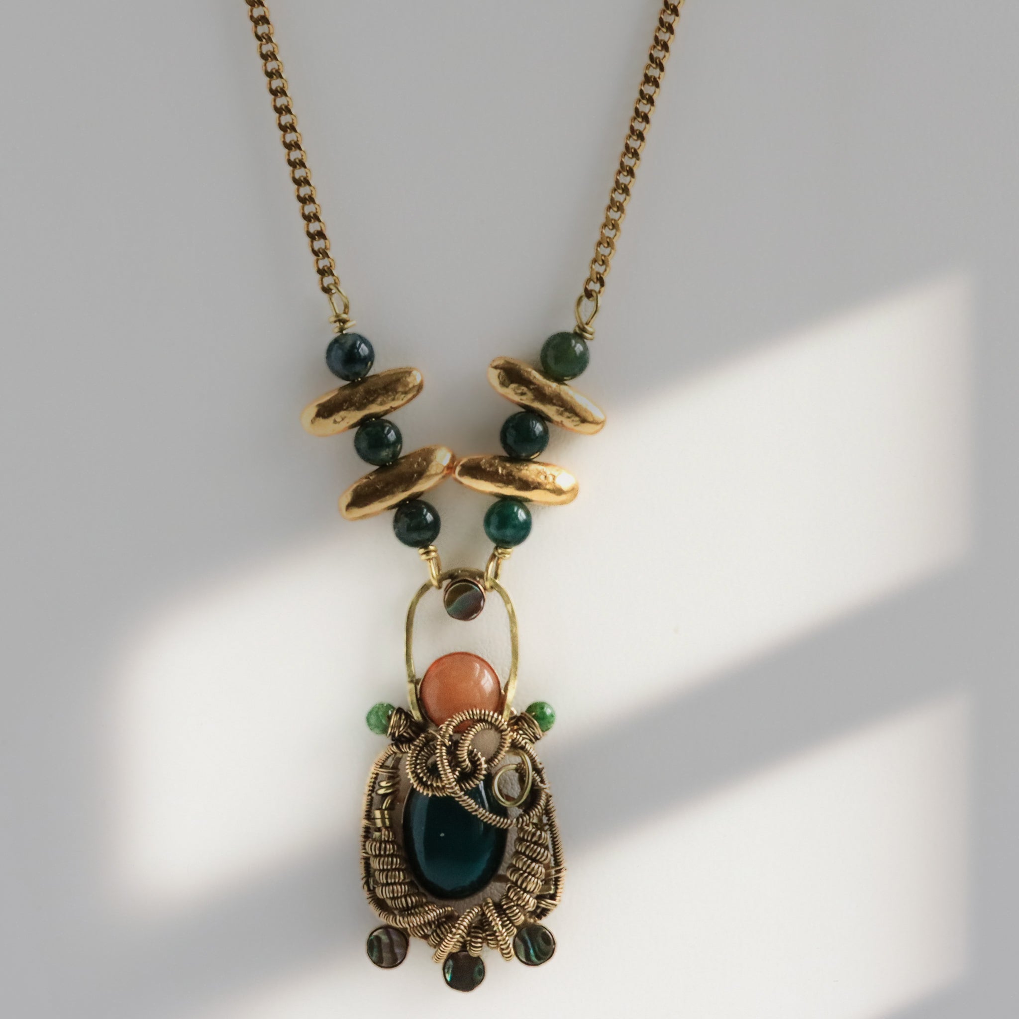 Close-up macro of hand wire-woven brass pendant with red aventurine and dark green jade cabochons and abalone shell accents, artisan metalsmith jewelry by bykjones