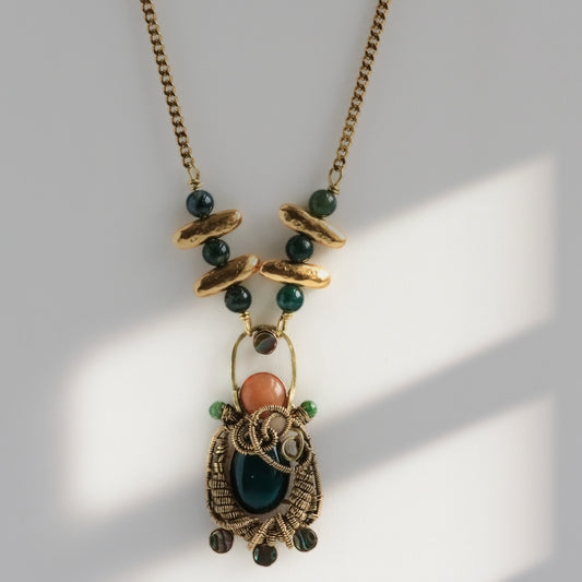 Close-up macro of hand wire-woven brass pendant with red aventurine and dark green jade cabochons and abalone shell accents, artisan metalsmith jewelry by bykjones