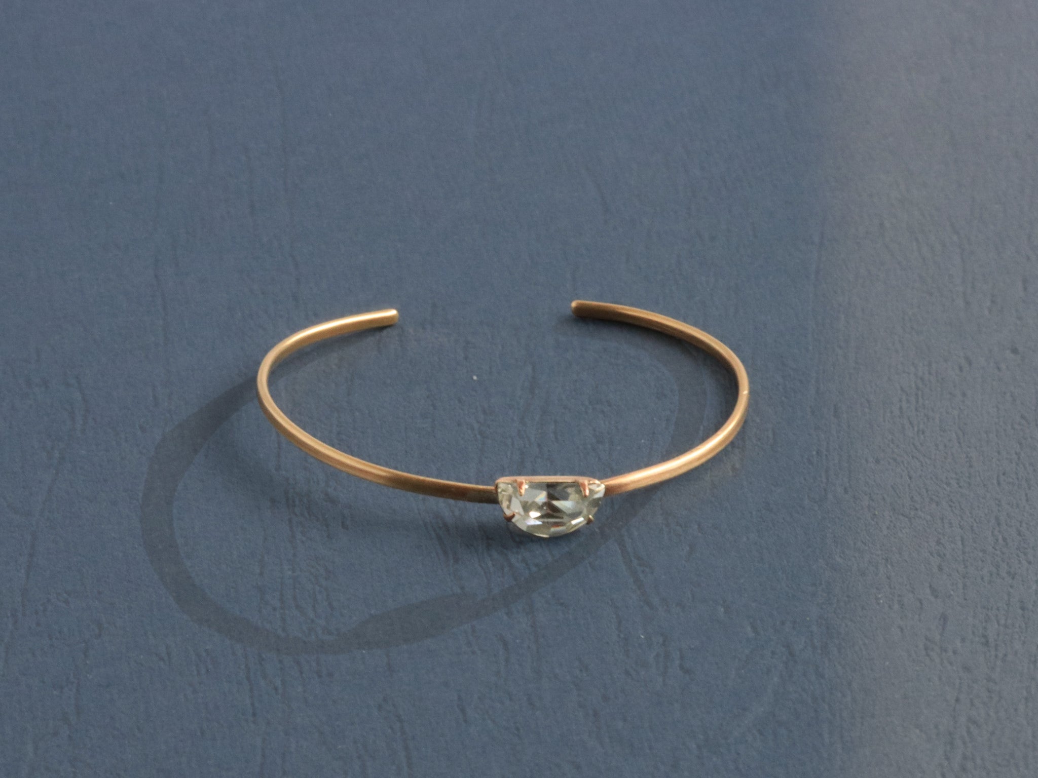 Side view of delicate hand-forged brass cuff bracelet showing thin wire profile and prong-set Swarovski crystal, artisan jewelry by bykjones