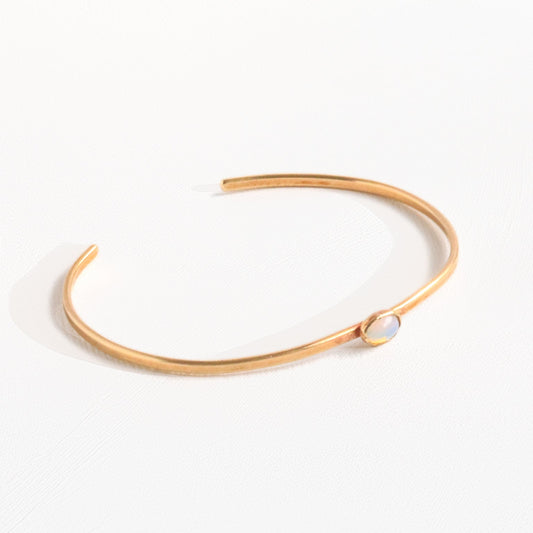 Handmade brass cuff bracelet with bezel-set opalite stone cabochon on warm linen background, dainty minimalist jewelry by bykjones NC