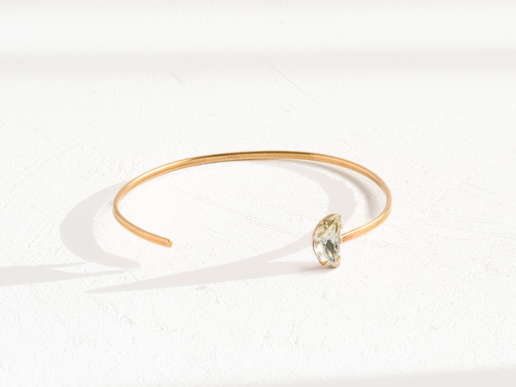 Handmade brass cuff bracelet with asymmetric off-center Swarovski clear crystal, overhead flat lay on white background, artisan jewelry by bykjones