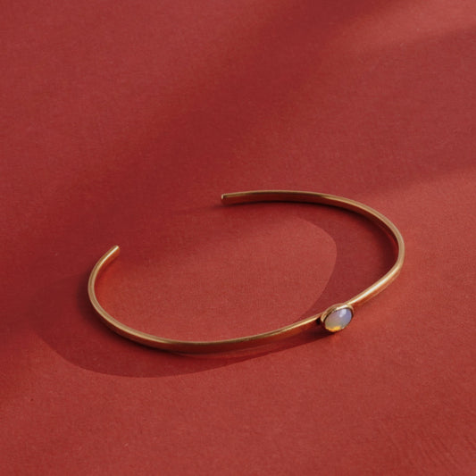 Handmade brass cuff bracelet with bezel-set opalite stone cabochon on warm linen background, dainty minimalist jewelry by bykjones NC