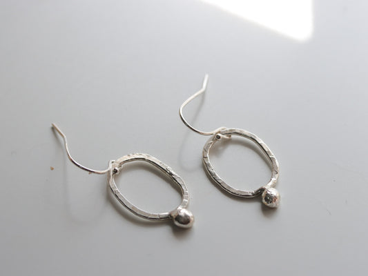 Minimalist artisan silver earrings on white textured background
