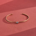 Load image into Gallery viewer, Close-up macro of opalite cabochon bezel-set in hand-forged brass cuff showing milky blue color shift, artisan gemstone jewelry by bykjones
