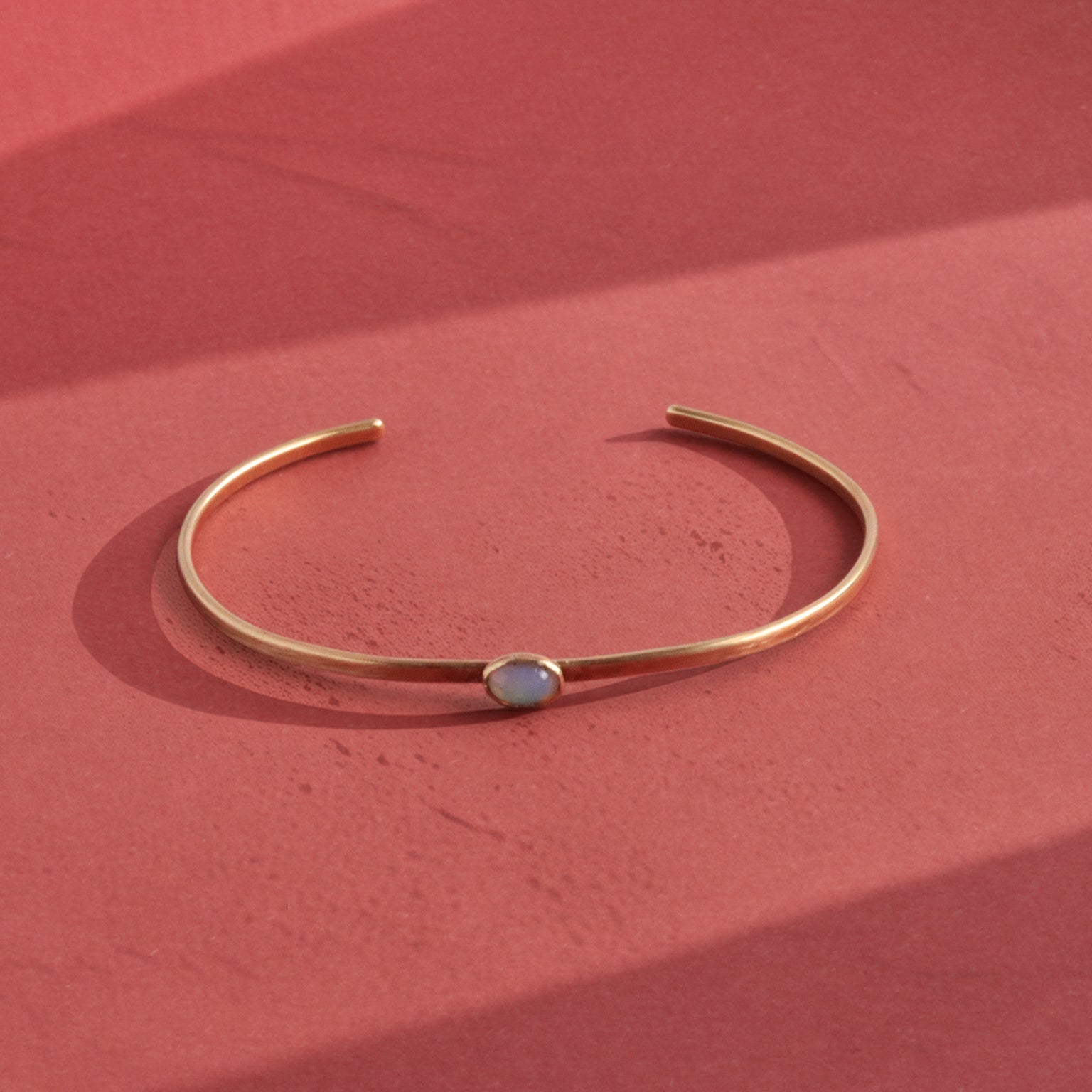 Close-up macro of opalite cabochon bezel-set in hand-forged brass cuff showing milky blue color shift, artisan gemstone jewelry by bykjones